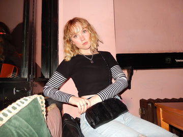 Woman in a striped top wearing a black textured crossbody bag on a chain strap during a night out
