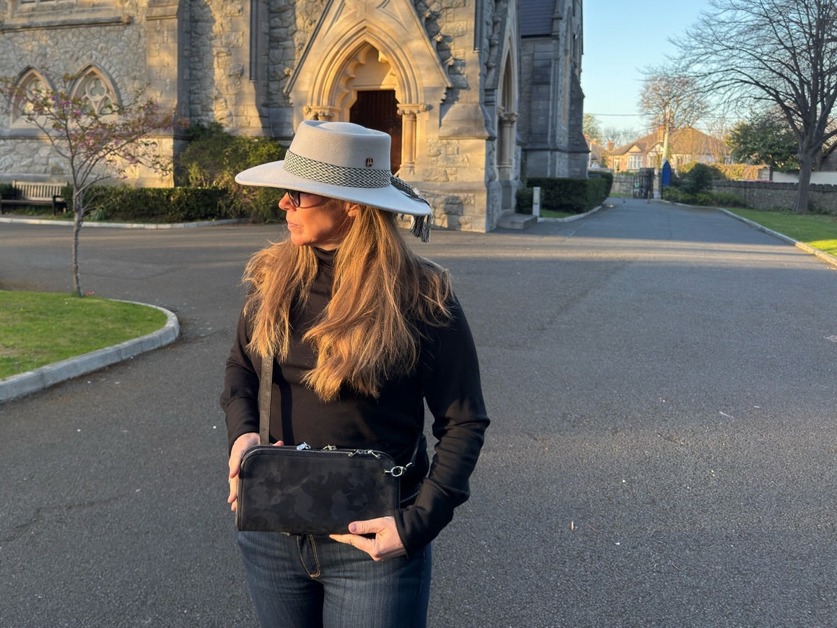 Vitale by Myriad founder MaBelle Bray wearing a black camo crossbody outside a stone church in golden evening light
