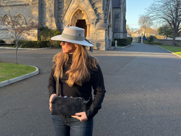 Vitale by Myriad founder MaBelle Bray wearing a black camo crossbody outside a stone church in golden evening light