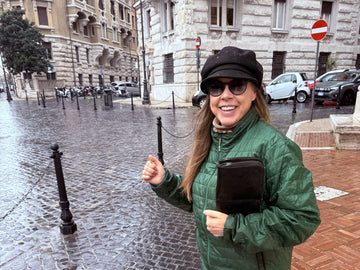 Vitale by Myriad founder MaBelle Bray smiling on a rainy cobblestone street, holding a black croc-textured clutch