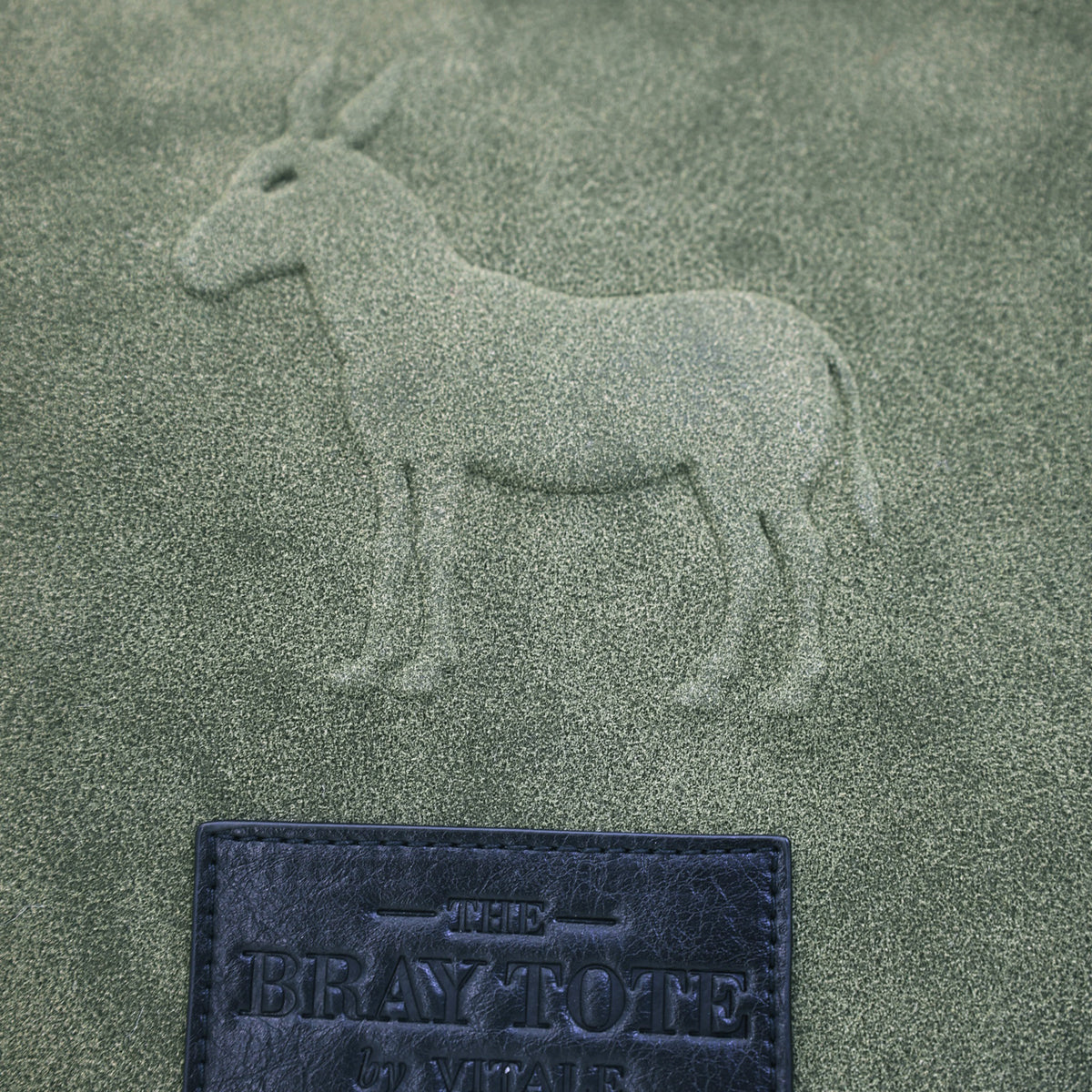 Close-up of the embossed donkey and logo tag on olive faux suede