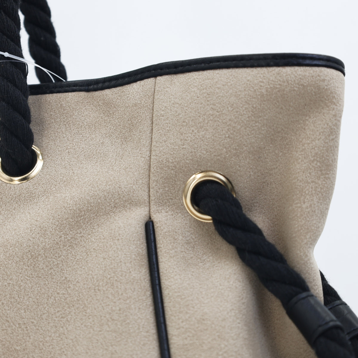Close-up of a gold eyelet and black twisted rope strap on the Bray taupe faux suede tote