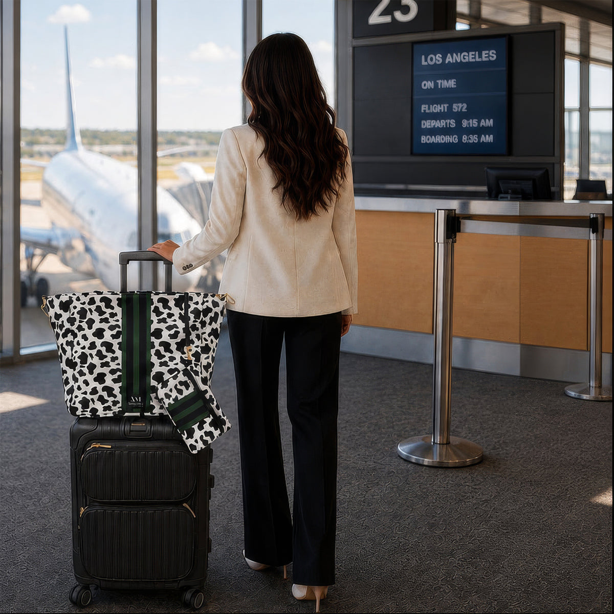 Woman at an airport gate with the Dublin cow print tote on her rolling suitcase