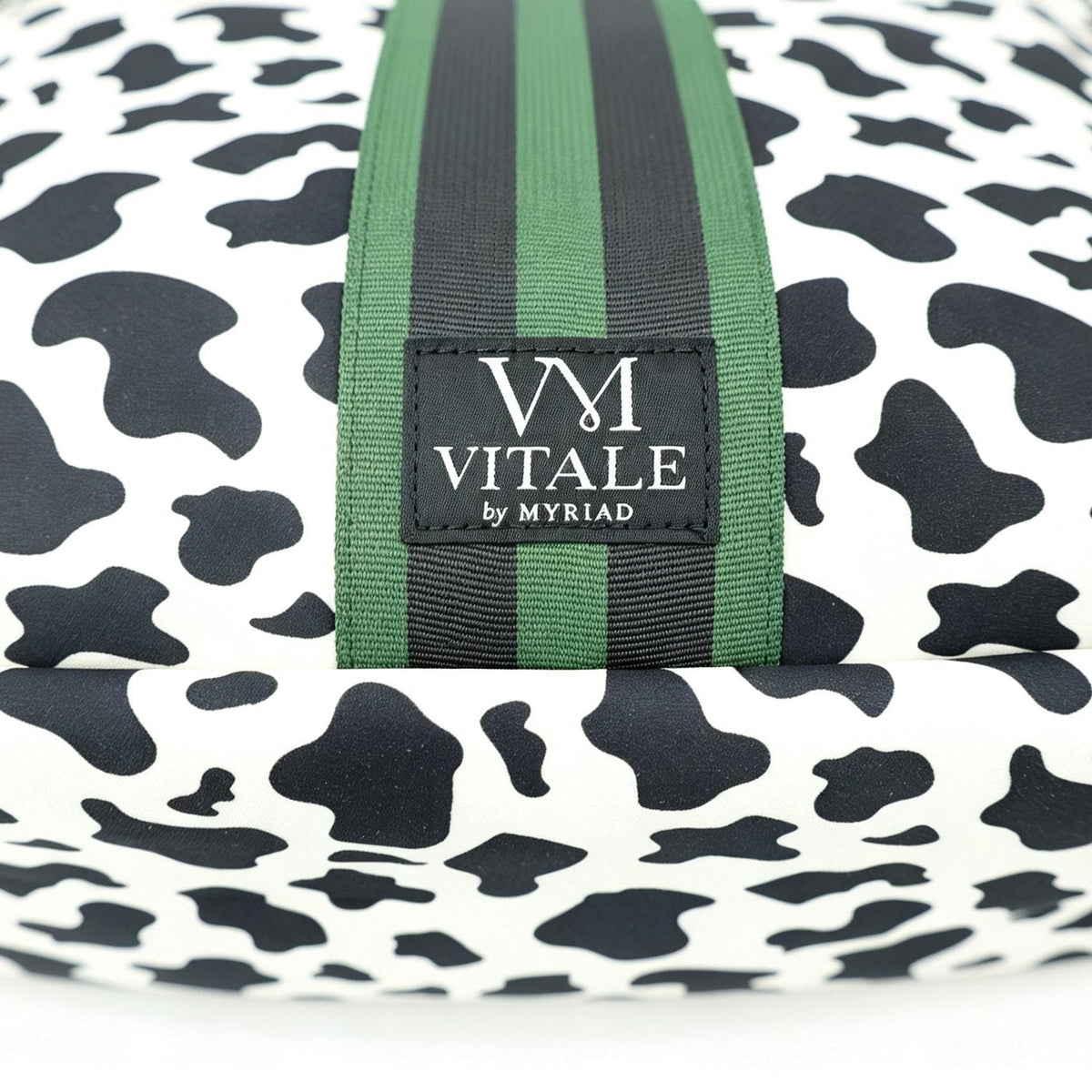 Close-up of the Vitale by Myriad logo tag on the green striped webbing of the Dublin cow print tote