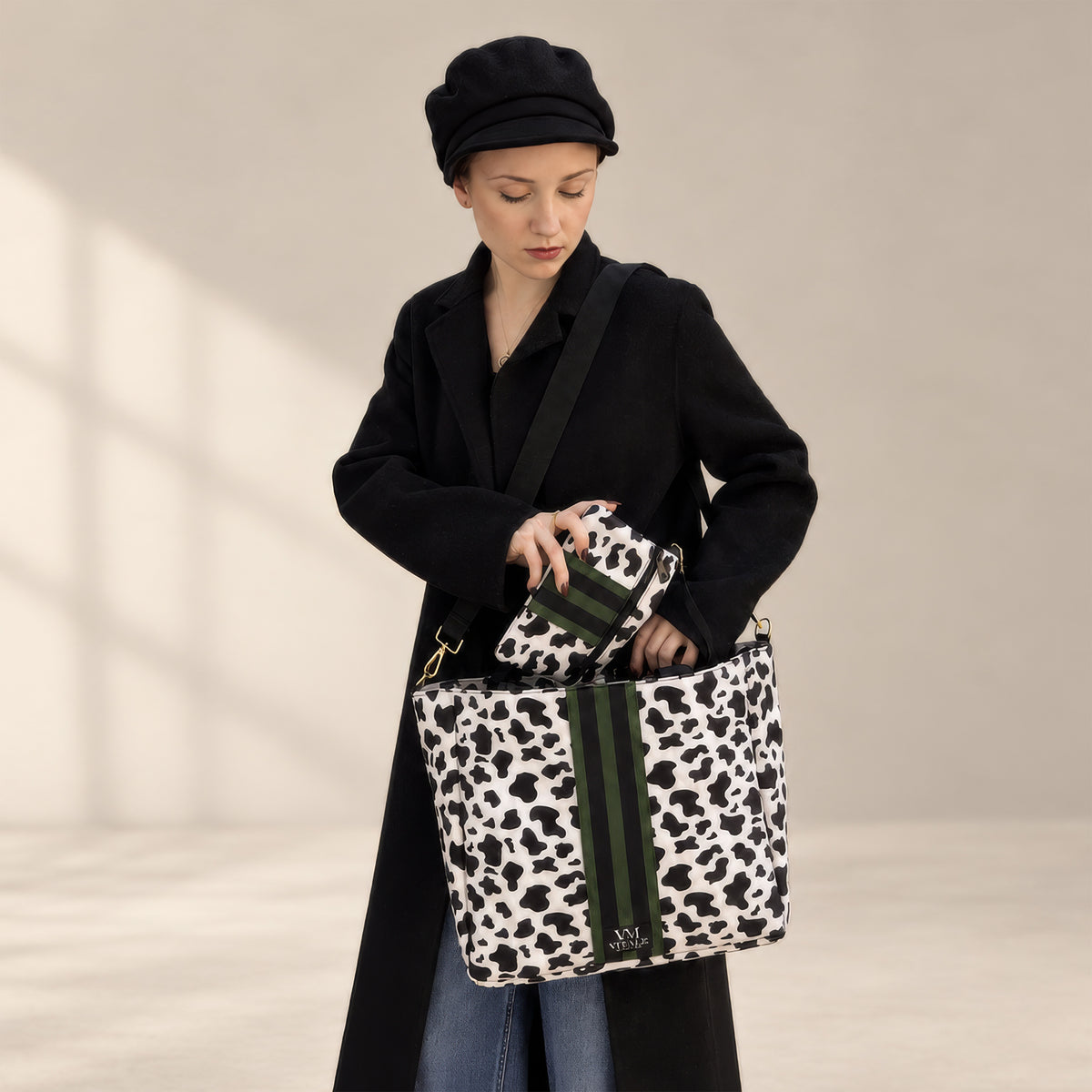 Woman in a black coat and beret carrying the Vitale Dublin cow print tote on her shoulder, holding the matching pouch