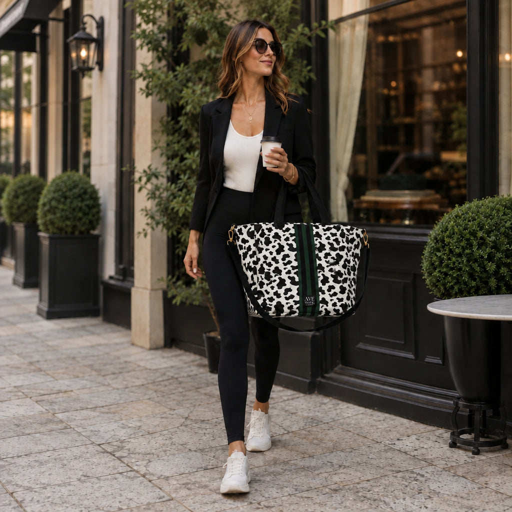 Woman in a black blazer carrying the Vitale by Myriad Dublin cow print tote on a city street with a coffee in hand