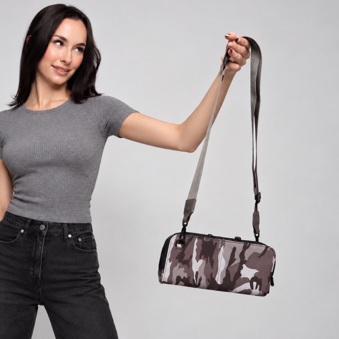 Woman holding up the Eros black camo RFID neoprene crossbody by its nylon strap