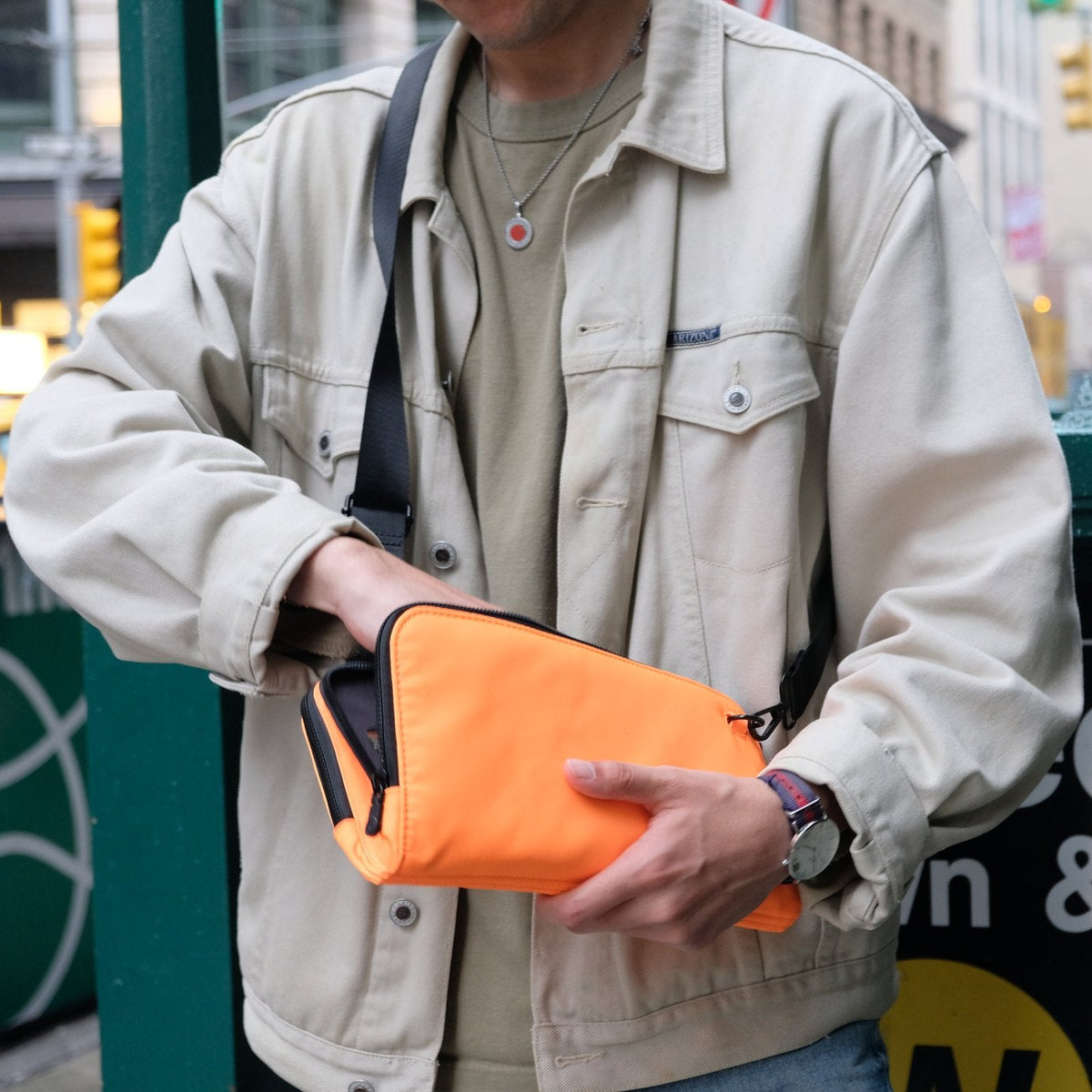 Man at a New York City subway entrance wearing the Eros orange nylon crossbody