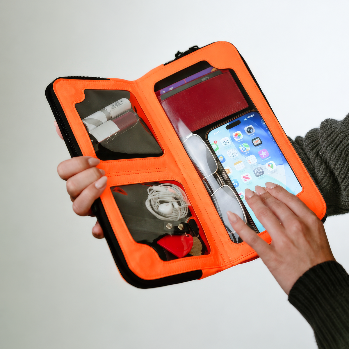 Hands using a phone through the touchscreen window of the open Eros orange nylon crossbody
