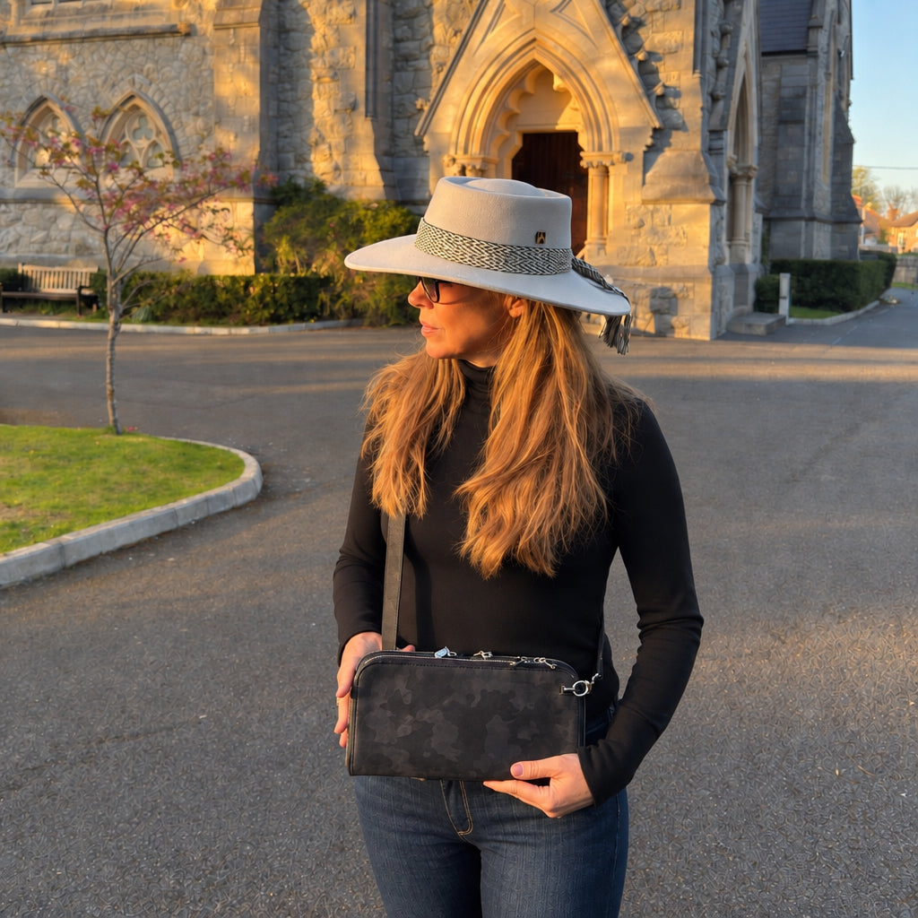 Founder MaBelle Bray wearing a Zeloso Black Camo leather clutch as a crossbody outside a stone church in evening light