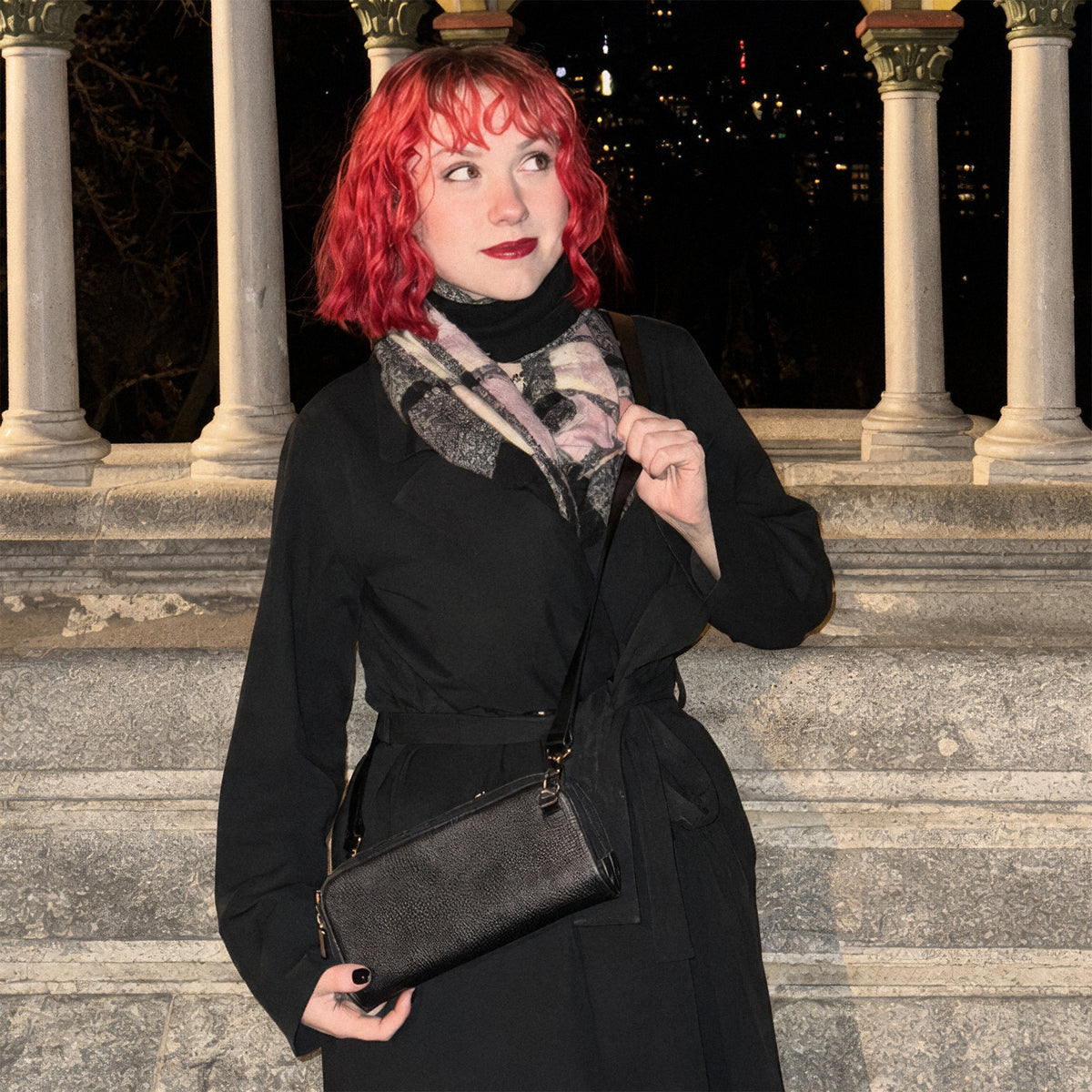 Woman in a long black coat wearing the Hestia black pebble mini crossbody at night