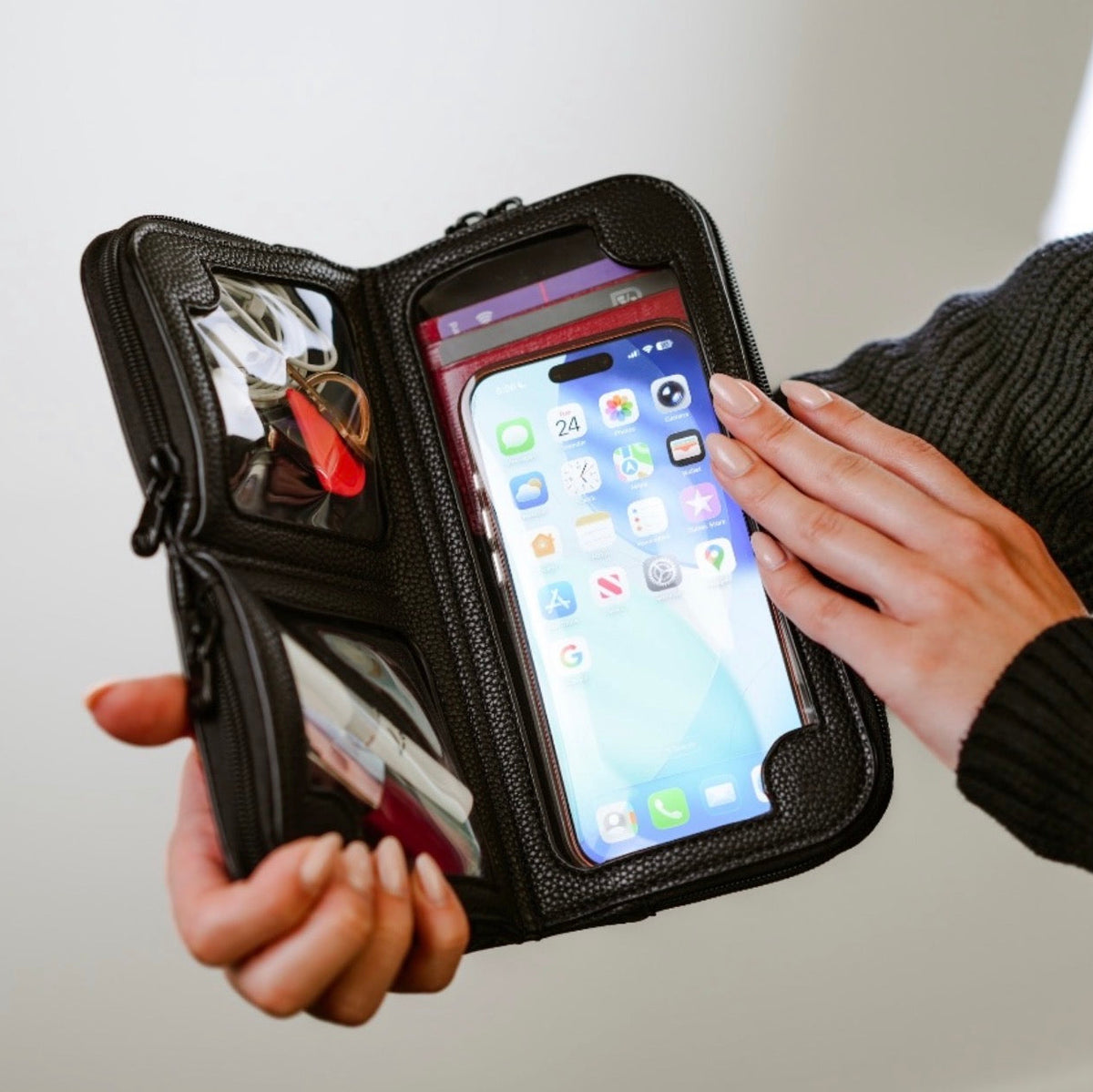 Hands holding the Hestia black pebble mini crossbody open, phone in the touchscreen pocket, cards and keys above