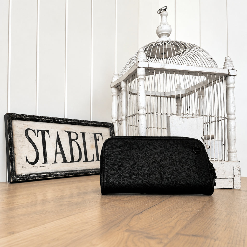 Hestia black pebble mini crossbody clutch on a wood floor beside a vintage stable sign and birdcage