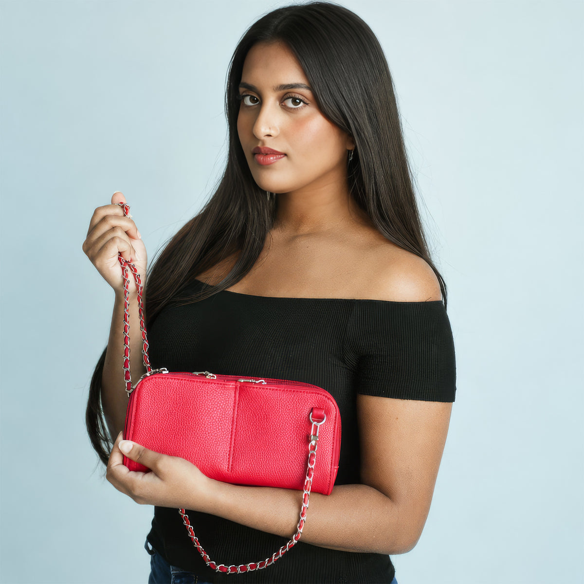 Woman in a black off-shoulder top holding a scarlet red Vitale by Myriad Hestia bag by its red and silver chain strap