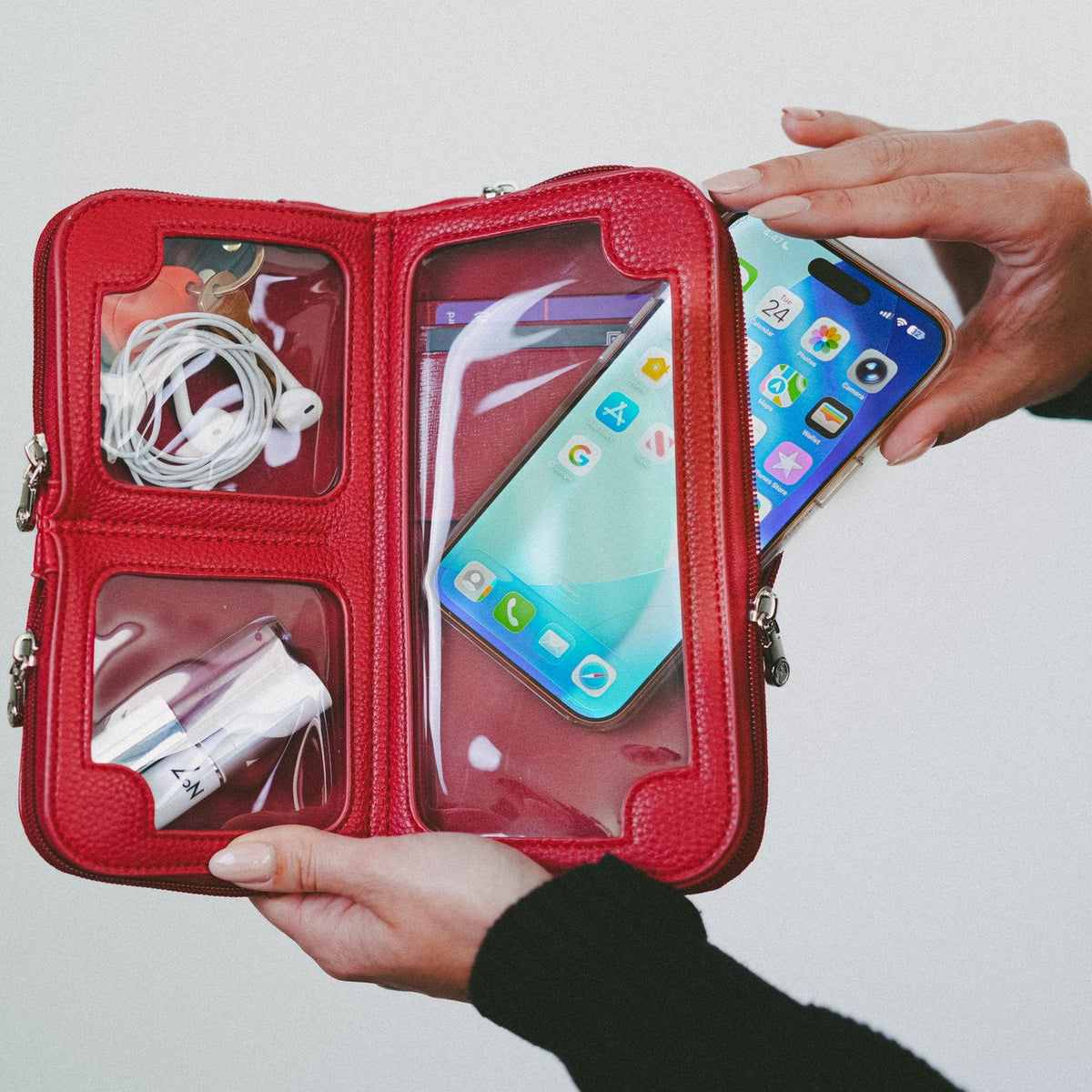 Hands holding the Hestia scarlet red mini crossbody open, phone in the touchscreen pocket, essentials in the top compartments