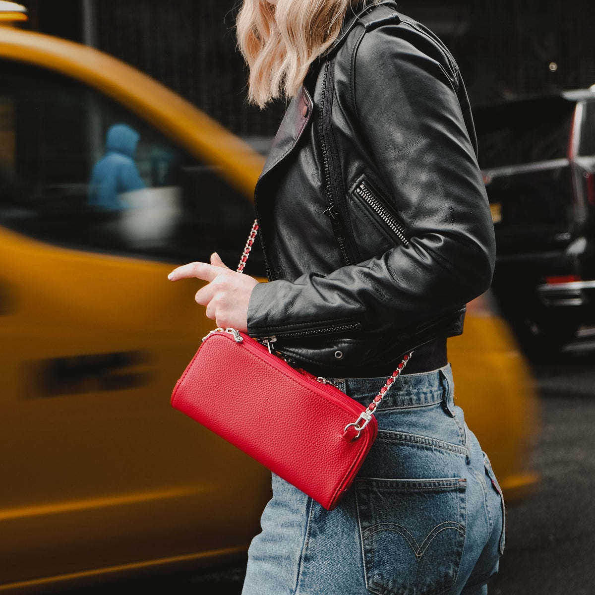 Hestia scarlet red mini crossbody worn with jeans and a leather jacket beside a yellow taxi