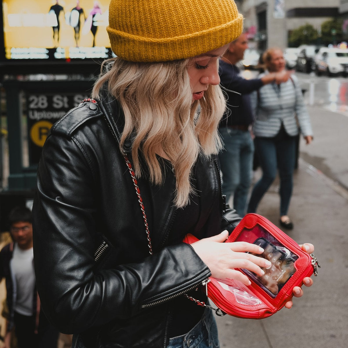 Woman in a yellow beanie using her phone through the touchscreen window of the Hestia scarlet red mini on a city street