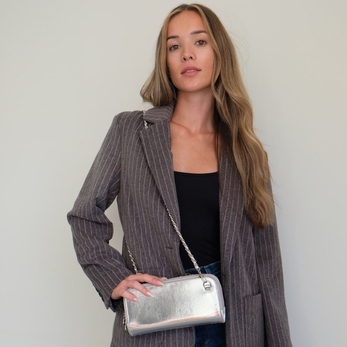 Woman in a gray pinstripe blazer wearing the Hestia silver metallic mini crossbody on its chain strap