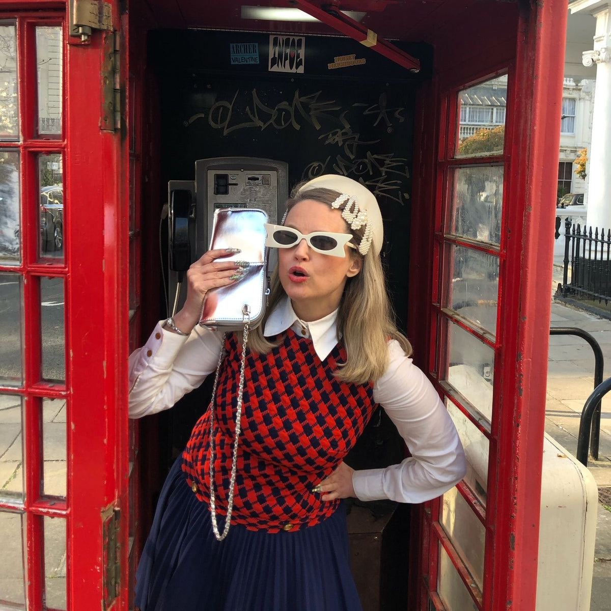 Woman in a red London phone booth with the Hestia silver metallic mini crossbody