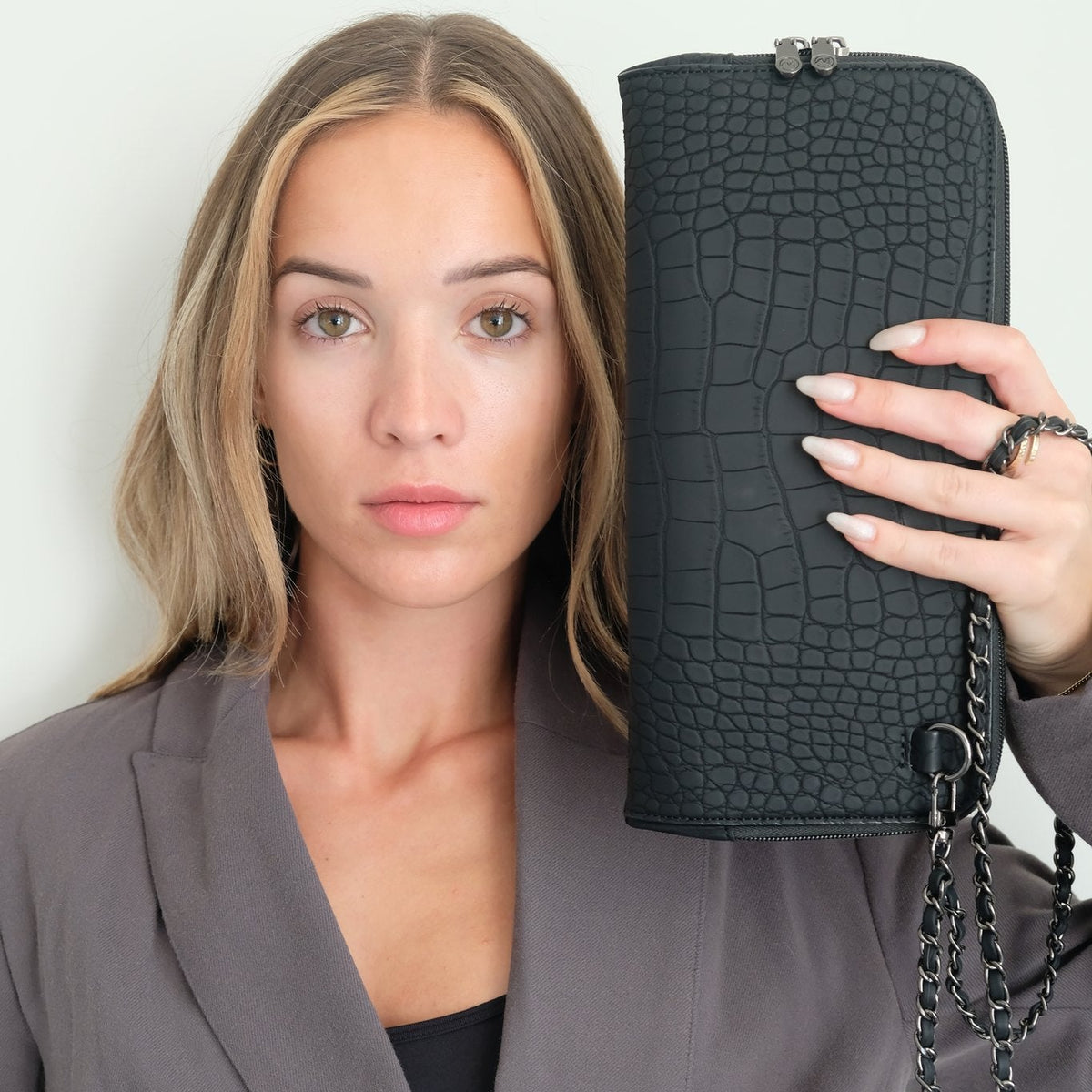 Woman holding the Osmand black matte croc crossbody up beside her face to show the croc-embossed texture