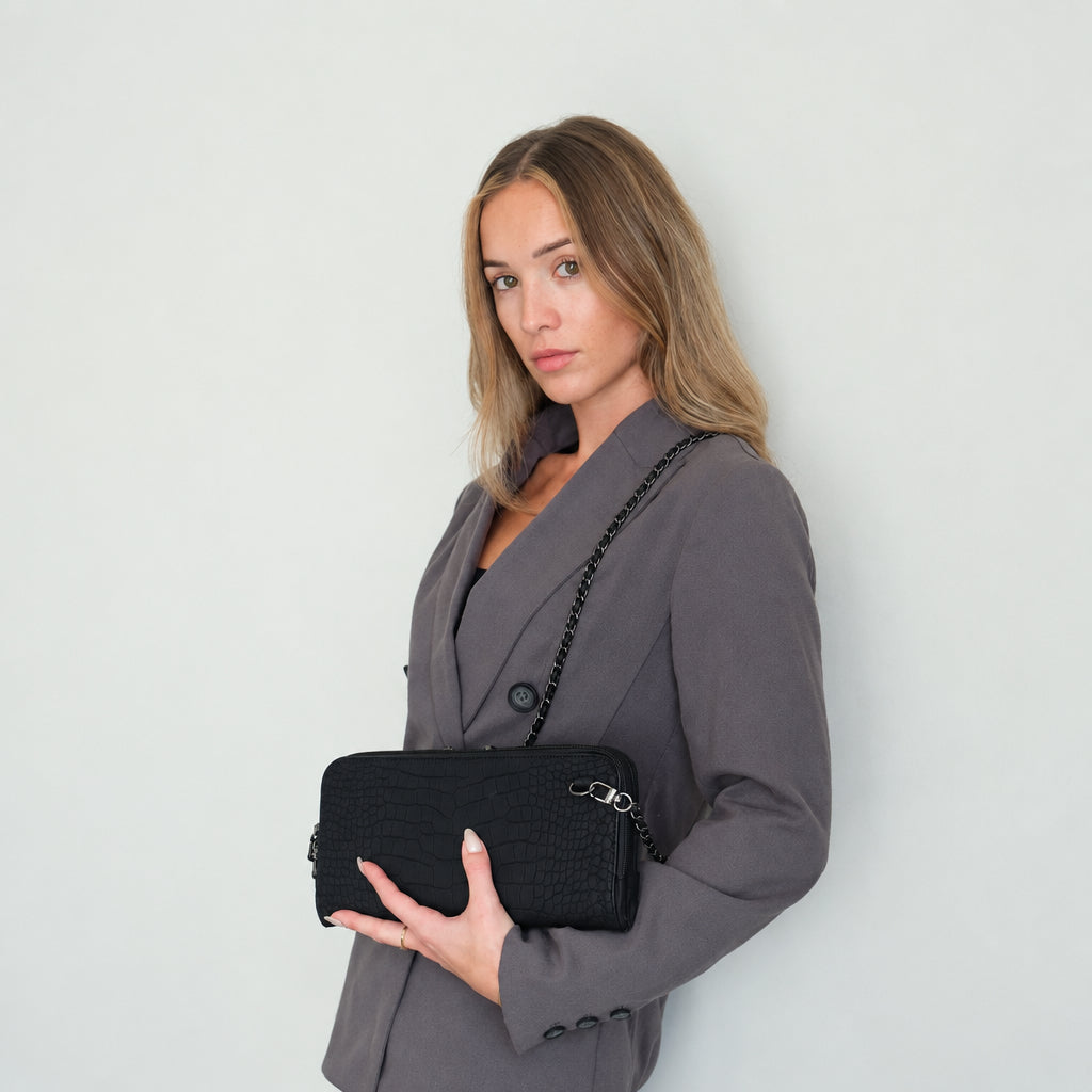 Woman in a gray blazer wearing the Osmand black matte croc as a crossbody on its chain strap