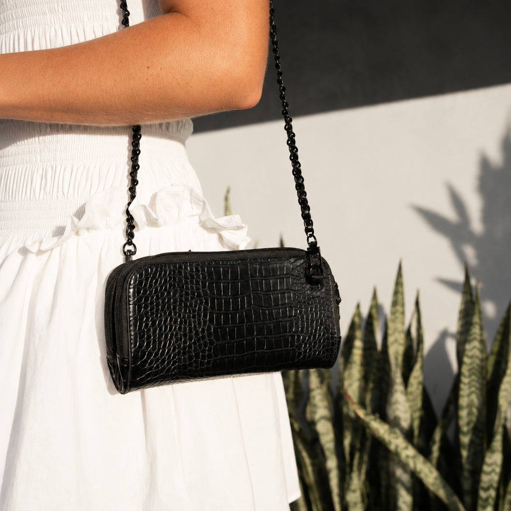 Close-up of the Osmand black shiny croc mini worn at the hip on its chain strap