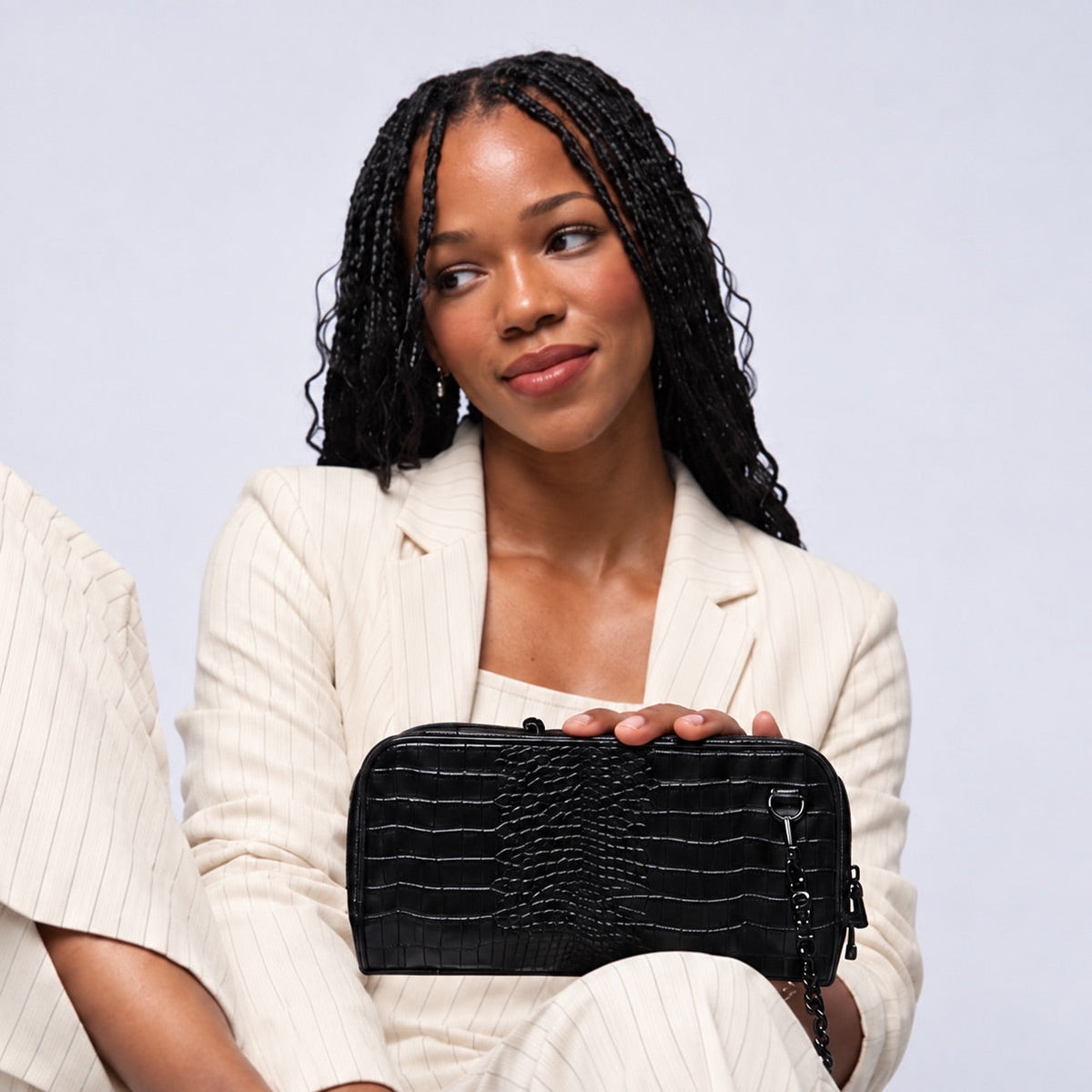 Woman in a cream suit holding the Osmand black shiny croc mini crossbody clutch