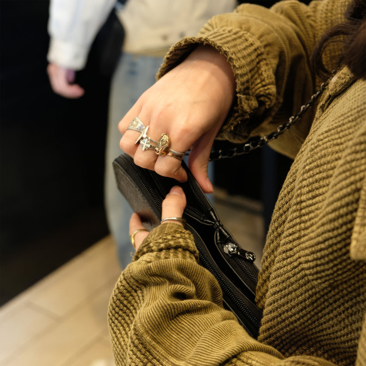 Hands reaching into the zippered compartments of the Petrel black snake mini crossbody clutch