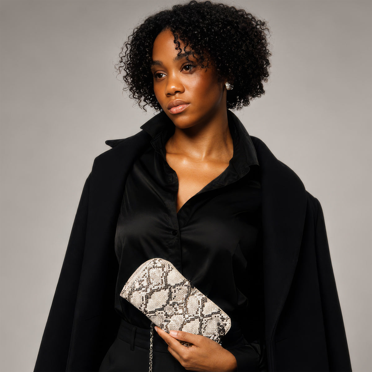 Model in a black blazer carrying the Petrel natural snake print mini crossbody clutch