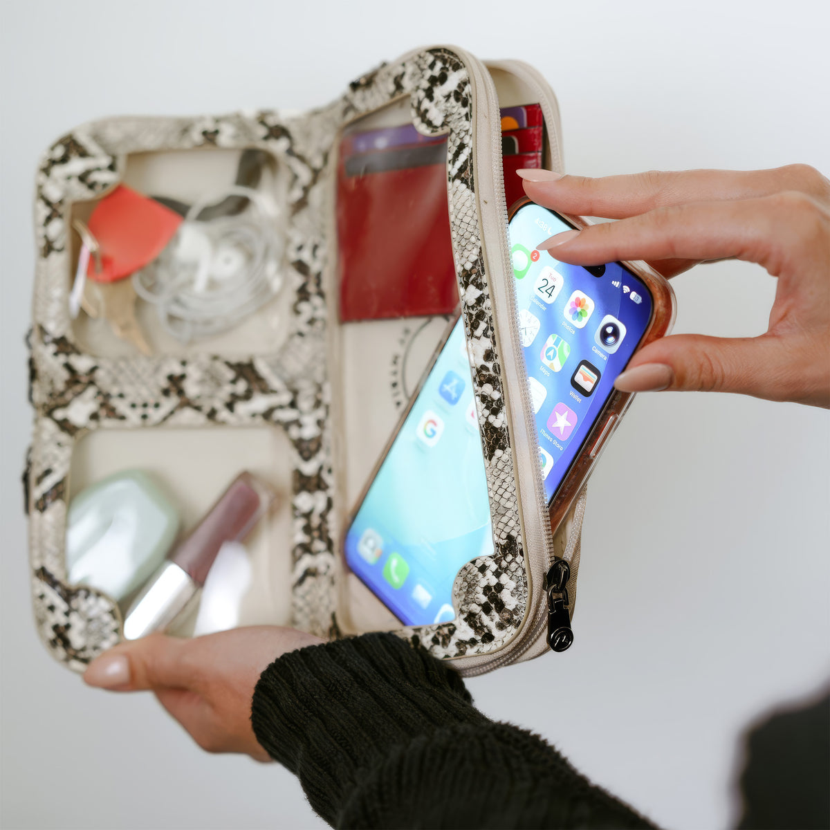 Woman using her phone through the touchscreen window of the Petrel natural snake mini crossbody clutch