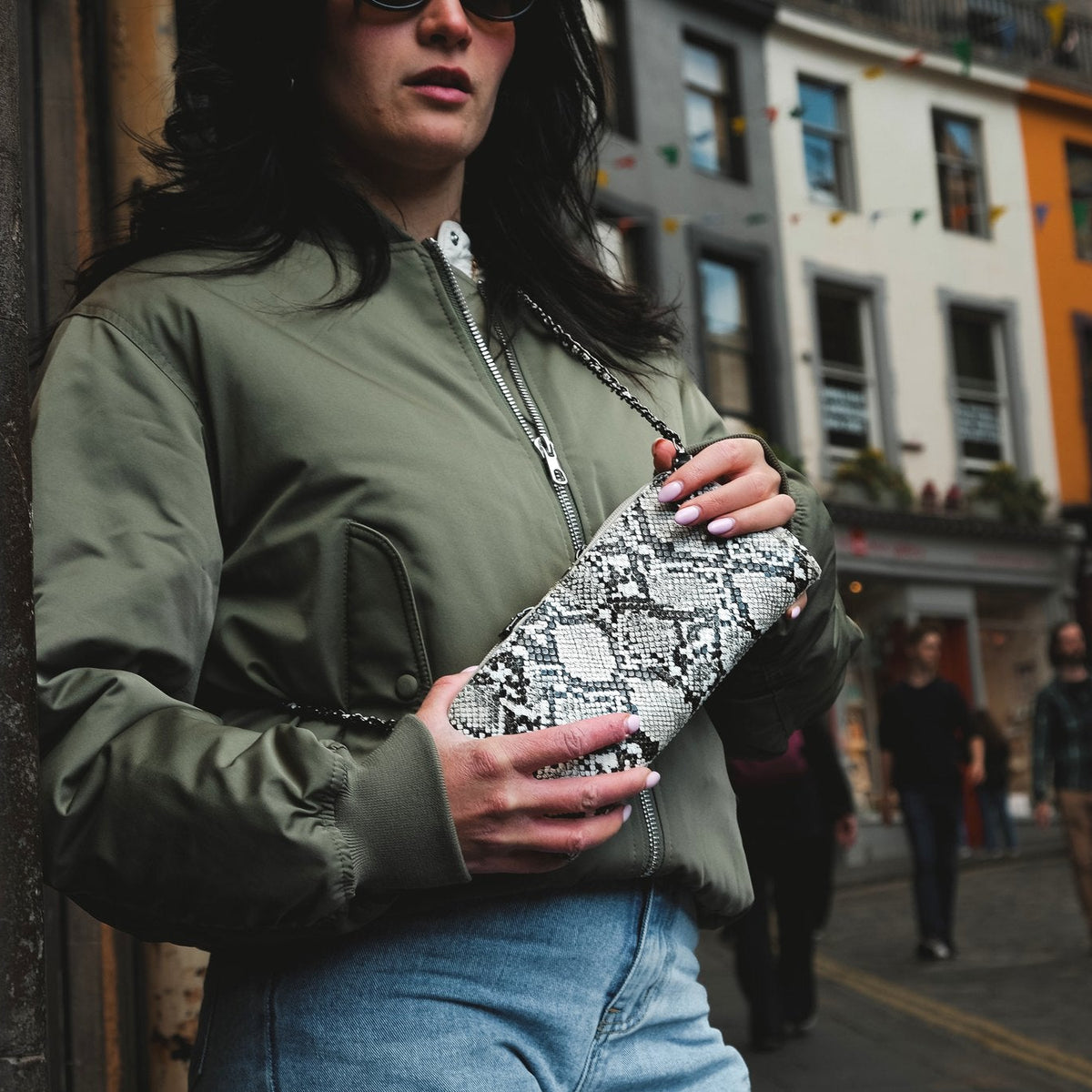 Woman wearing the Petrel natural snake mini crossbody bag on its chain strap on a city street