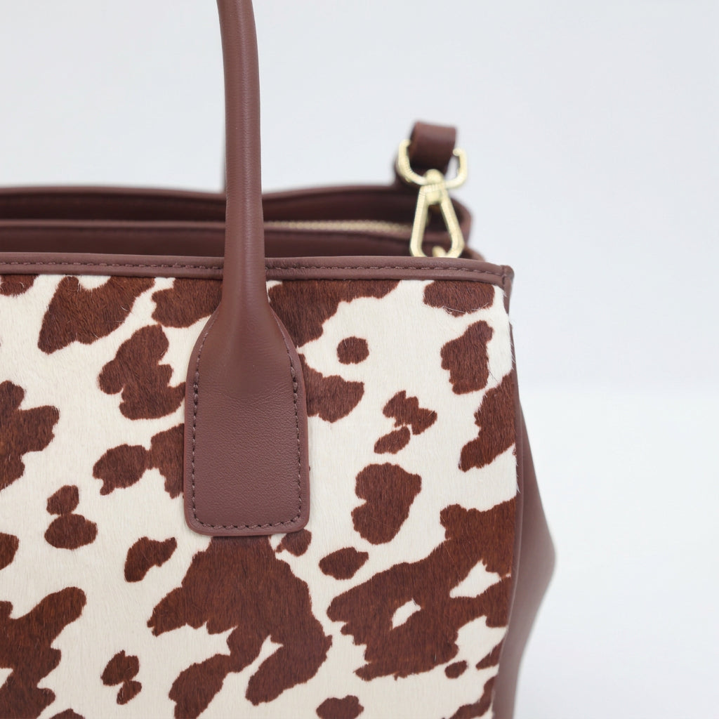 Close-up of the Roma tote's cow hair-on-hide panel, brown leather handle and strap clip