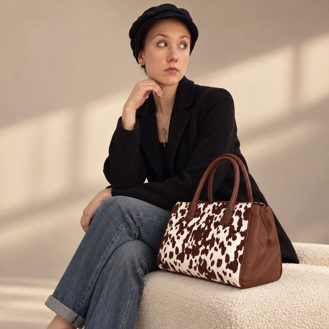 Woman in a black blazer and cap seated with the Roma brown cow hair-on-hide tote