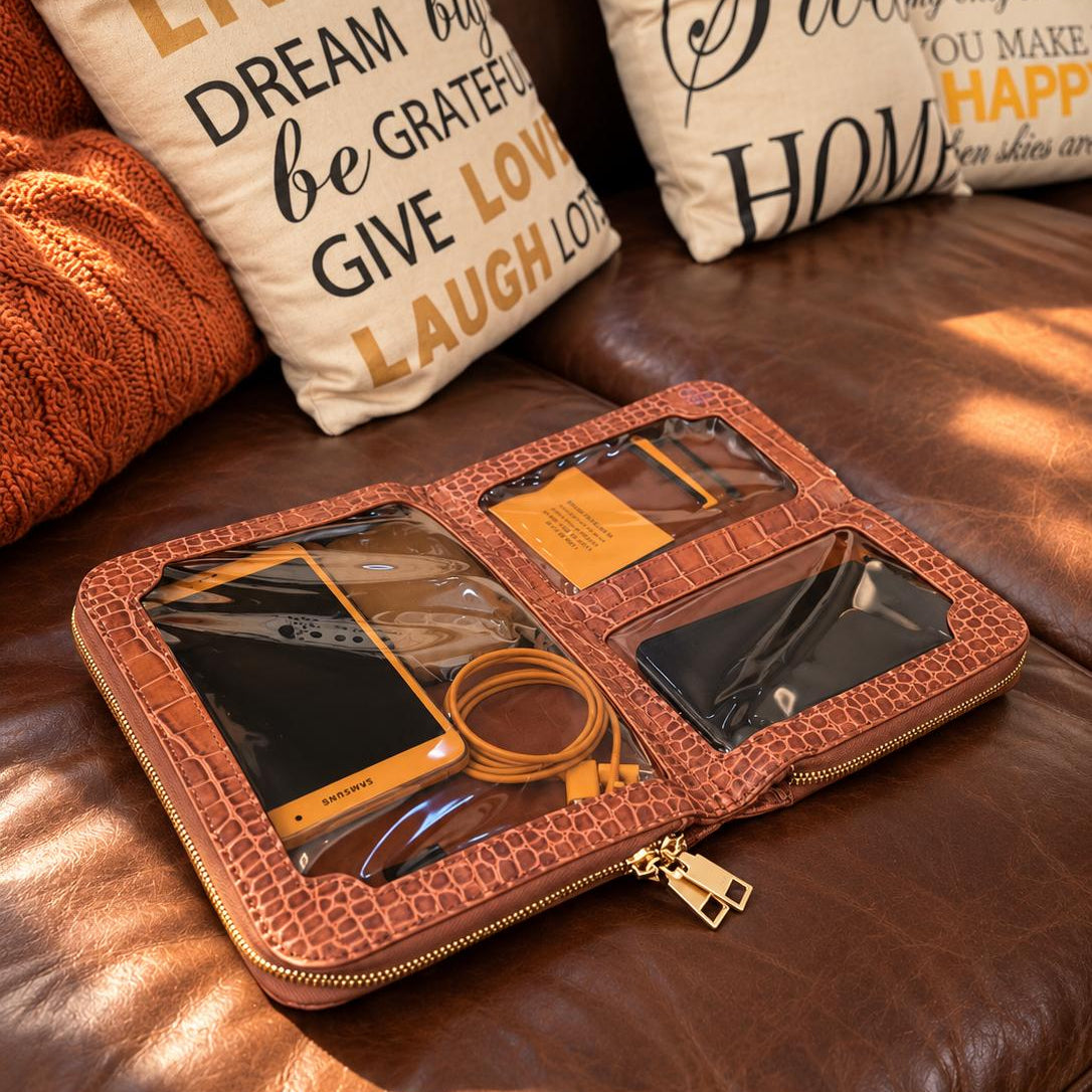 Vallina croc-embossed crossbody in cognac open flat on a leather sofa, showing its clear interior windows