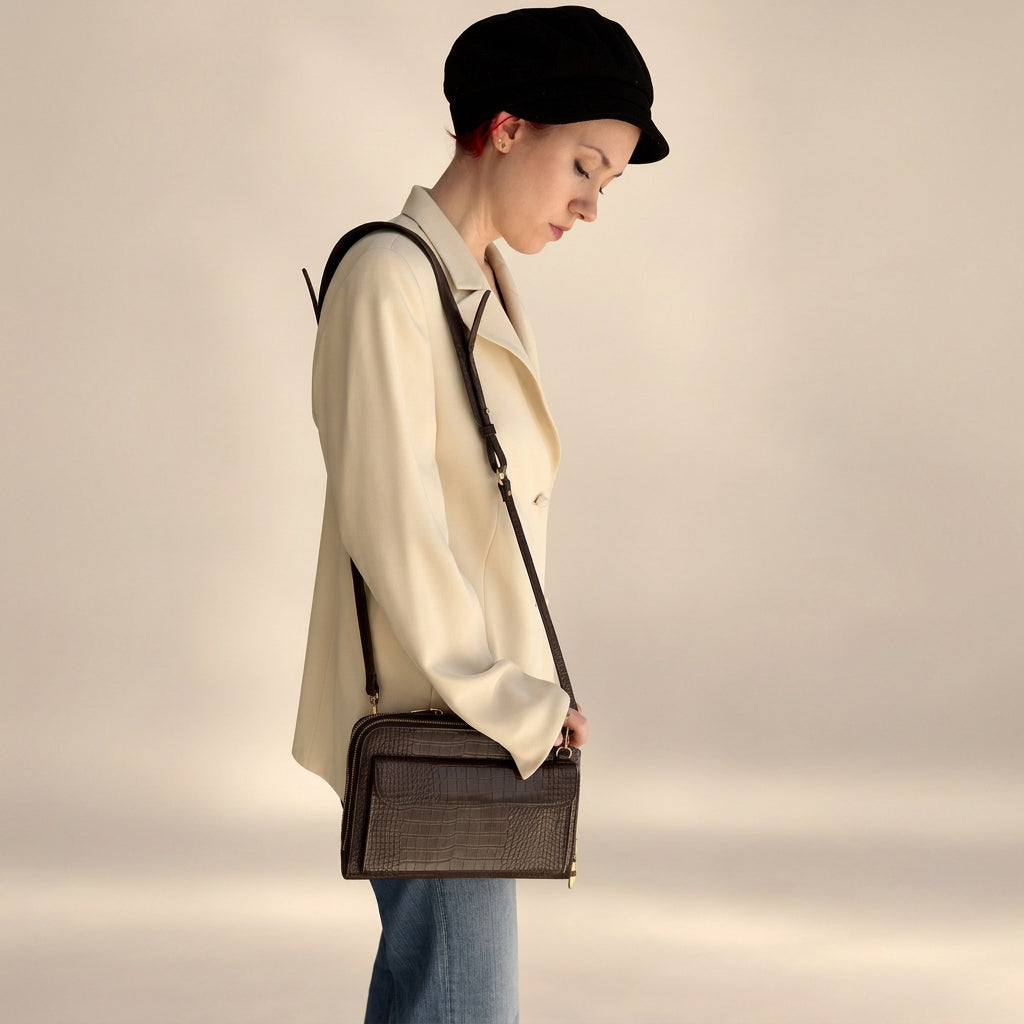Woman in a cream jacket and cap, seen from the side, wearing the Vallina croc-embossed crossbody in mocha