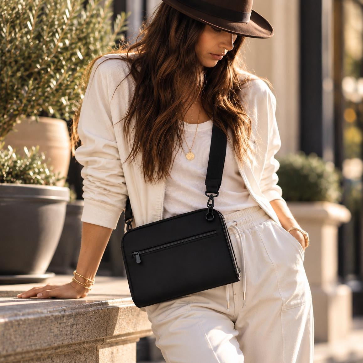 Woman in a hat and cream outfit wearing the Vallina black neoprene crossbody across her body